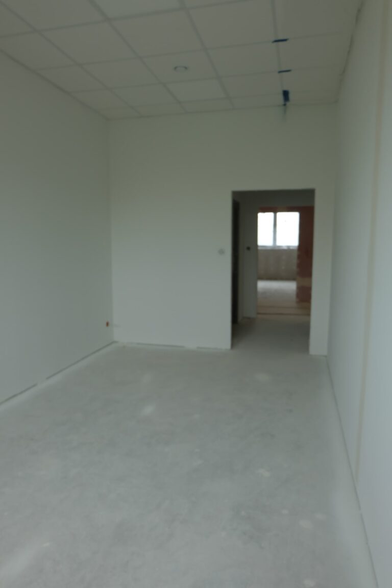 Na zdjęciu jest pokój z białymi ścianami i wejściem bez drzwi. Pokój jest w remoncie.