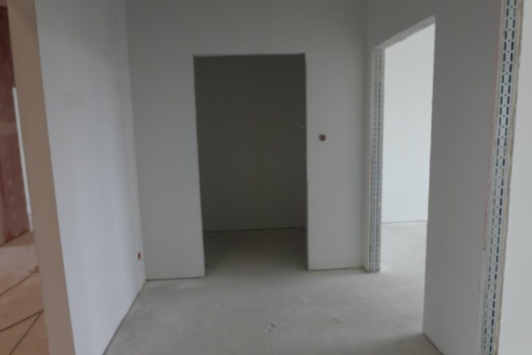 Na zdjęciu widać pokój w remoncie. Ściany są białe. Na wprost i po prawej stronie znajdują się wejścia do pokoi, w ktorych nie ma wstawionych drzwi.