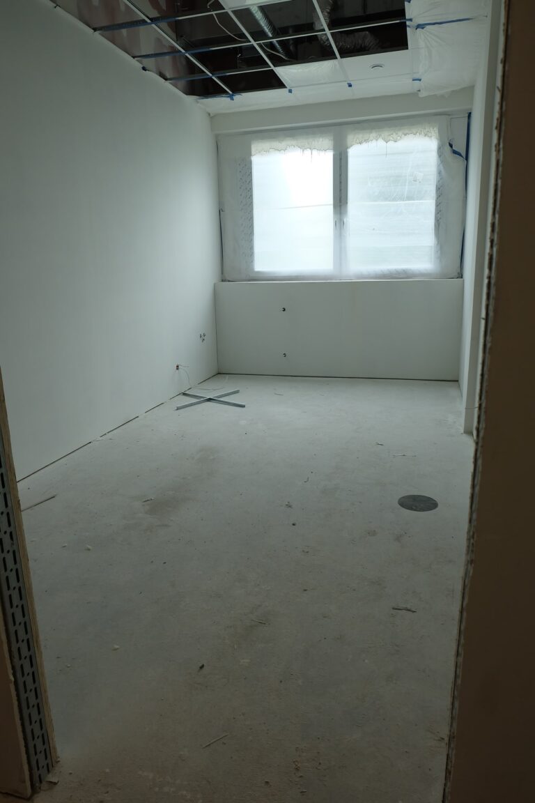 Na zdjęciu jest pokój z białymi ścianami i oknami wzdłuż jedej z nich. Pokój jest w remoncie.