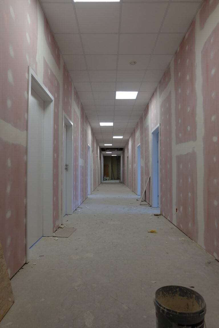 Na zdjęciu widać korytarz w czasie remontu. ściany są w gładzi. na podłodze leży wiadreko