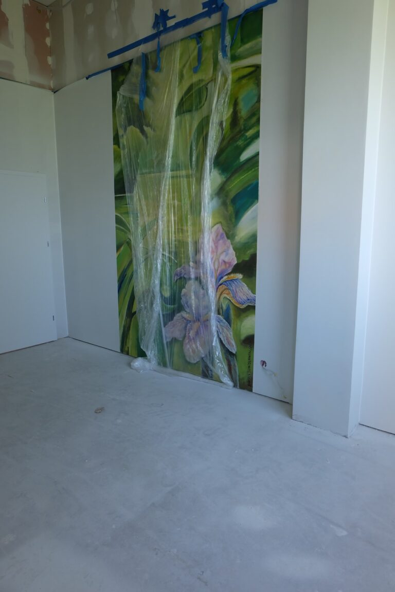 Na zdjęciu widać fragment pokoju w remoncie. Na jednej ze ścian jest namalowany duży zielony obraz z kwiatami. Jest on jeszcze w folii.