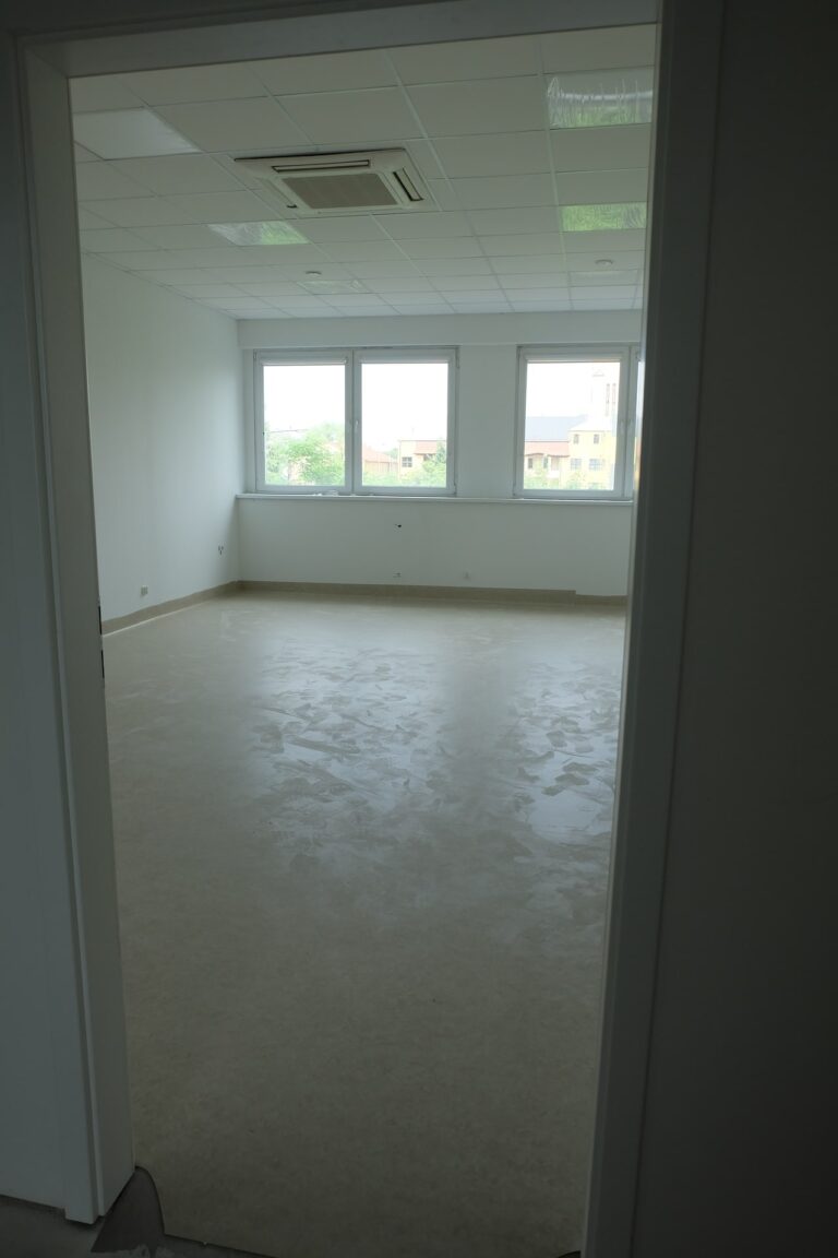 Na zdjęciu przedstawiony jest pokój z białymi ścianami i oknami naprzeciwko wejścia. Pokój jest w remoncie.