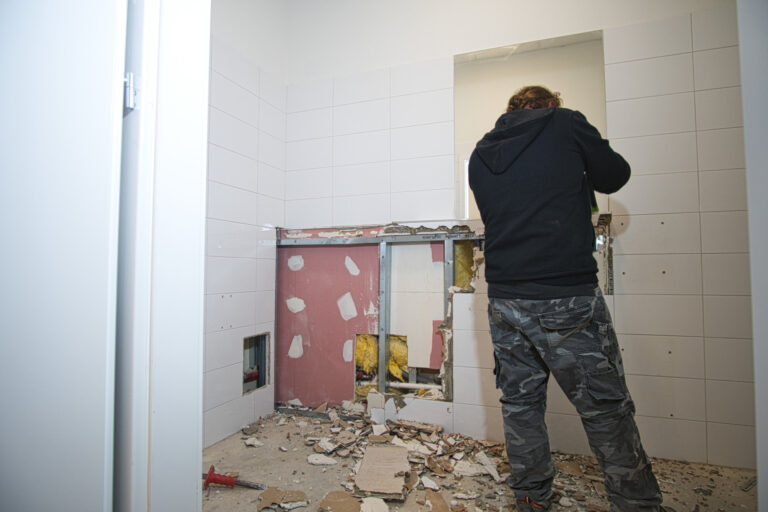 Na zdjęciu widać łazienkę w czasie remontu. Po prawej stronie widać pana robotnika od tyłu który kuje kafelki