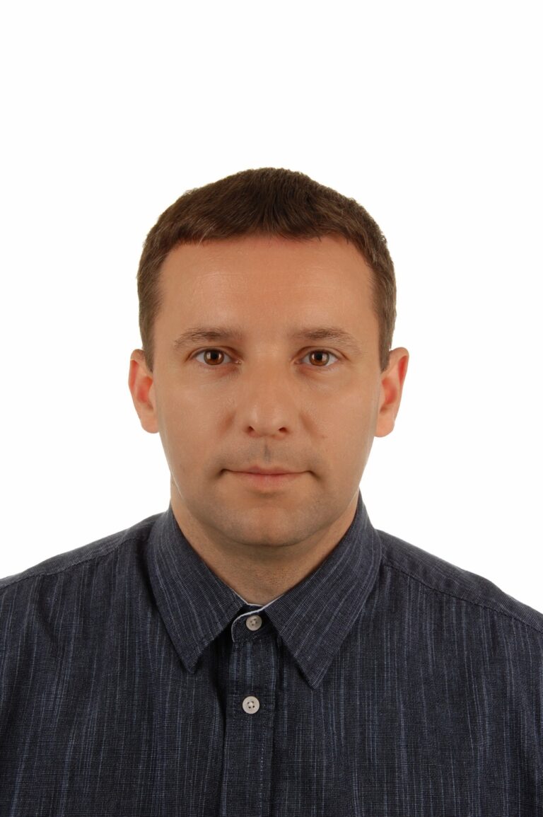 Na białym tle jest Pan Rafał Bugaj. Mężczyzna jest lekko uśmiechnięty. Ubrany jest w granatową koszulę.